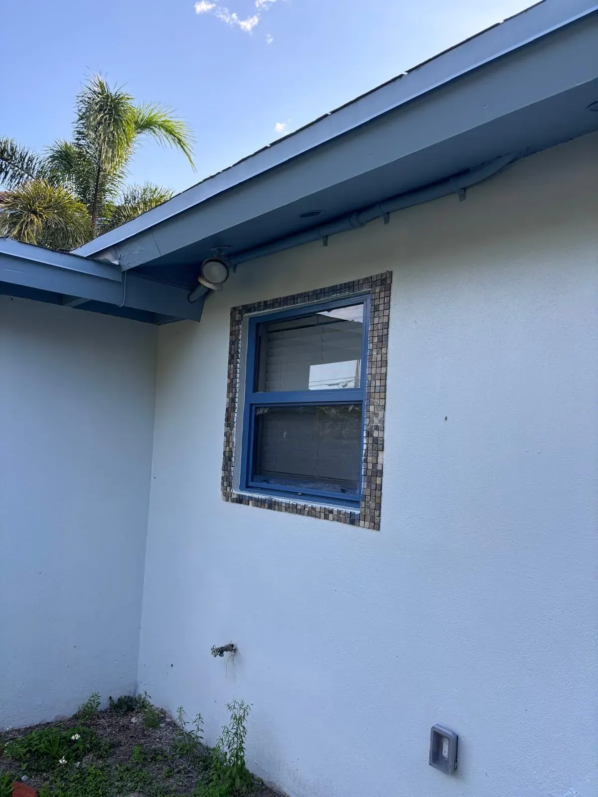 Exterior window with a mosaic tile surround and blue trim by JC General Painting in South Florida